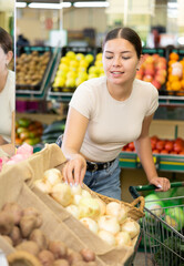 In modern supermarket,middle-aged woman carefully chooses garden onion from bag and puts in shopping cart