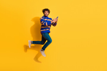 Full size photo of pretty young male running hold device wear trendy blue striped outfit isolated on yellow color background