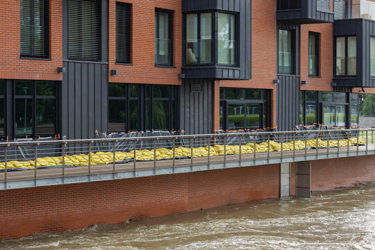 Flood protection measures with yellow sandbags and plastic sheeting safeguard a modern brick building along the riverside. Defense against high water levels and flood damage in an urban environment