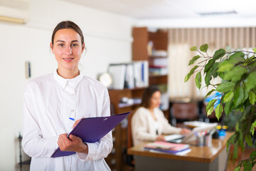 Cheerful american secretary woman in office holding clipboard with papers document write notes