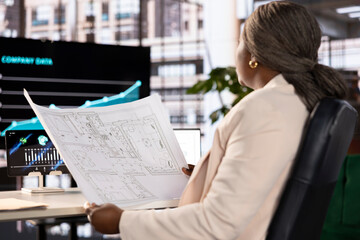 Architect looking over construction blueprint, ensuring compliance with local building codes and...