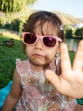 Little girl with sunglasses eating and making stop sign with hand