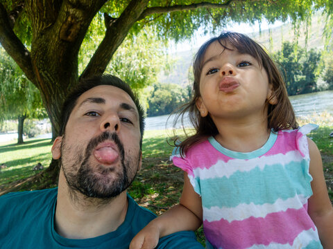 Father and daughter sticking out tongues in park