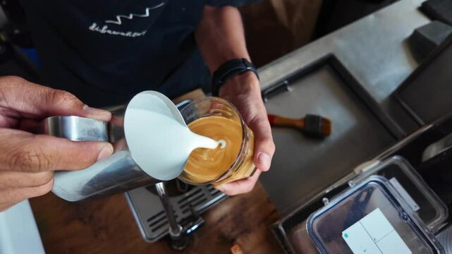 Barista making cappuccino. Barista pouring milk in cap and doing cappuccino art in coffee shop