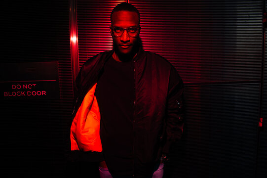 Man in black jacket with red lining under neon red lighting.
