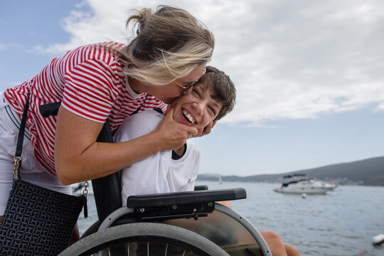 Mother hugs and kisses his disabled son by the sea