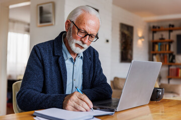 Senior man wearing eyeglasses writing in diary at home
