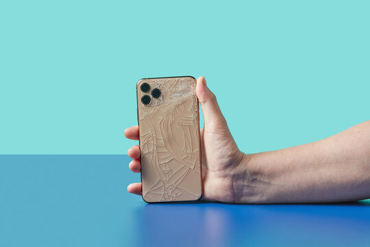 Gadget with shattered back panel in hand on blue studio surface