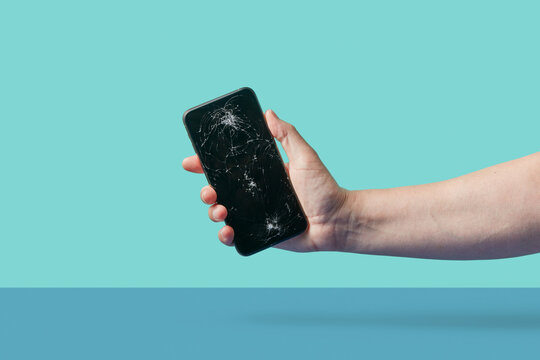 Person showing black smartphone with crashed display in studio