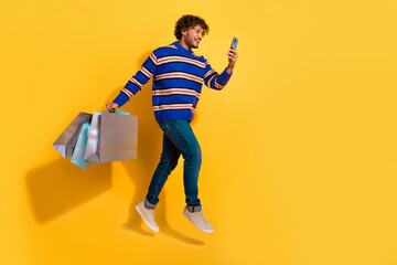 Full size photo of pretty young male hold gadget shopping bags running wear trendy blue striped outfit isolated on yellow color background