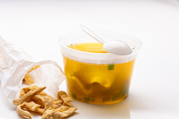 Clear plastic container of wonton Chinese soup next to pile of asian crackers