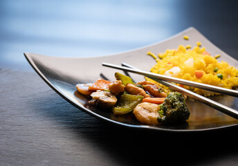 Traditional Chinese dish Hunan chicken with vegetables served with fried rice on black plate.