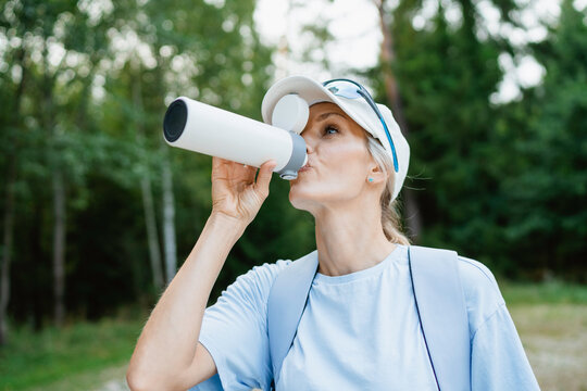 A woman drinks water while hiking in the forest