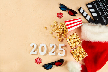 Happy New Year 2025 and Merry Christmas. Popcorn in cardboard boxes with white and red stripes, Santa Claus hat, wooden numbers 2025, 3D glasses for watching Christmas movies, clapboard. Top view 
