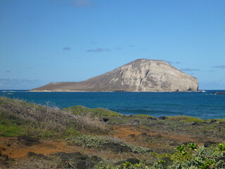 Beautiful view across the ocean of a rocky island on a bright sunny day, orange soil and vegetation