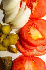 Sliced-up pickles, tomatoes, and onions on a white plate 