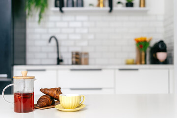 A cozy breakfast setup with tea, croissants, and a yellow cup in a modern kitchen
