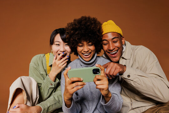 Three friends laughing together while looking at a smartphone