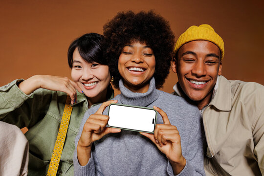 Three friends smiling and showing smartphone with empty screen