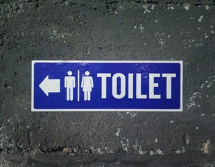 A Dark Blue Toilet Sign with White Writing on a Black Cement Wall