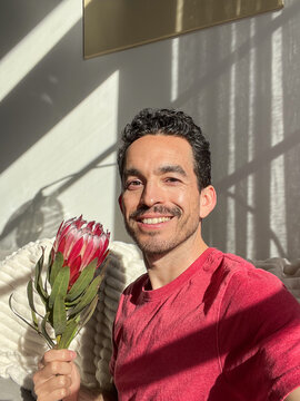 Man smiling holding a protea flower in natural light