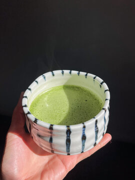 Hand holding a cup with green matcha beverage inside it
