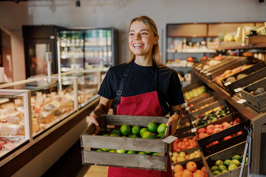 A proud and enthusiastic employee is showcasing a basket of fresh limes in a grocery stores lively produce section