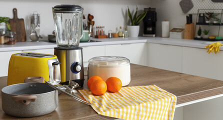 Blender, toaster, juicer, oranges and cooking pot on wooden table in kitchen
