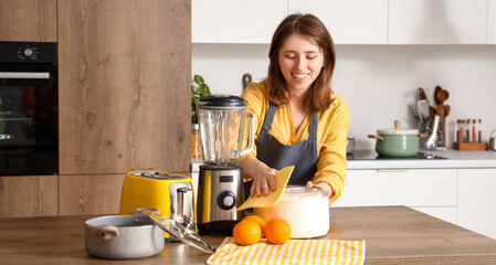 Young woman in kitchen cleaning juicer on wooden table