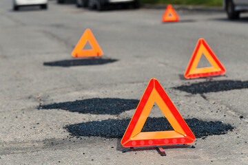 Road maintenance in progress with asphalt patches and warning signs. Temporary road repair. Fresh asphalt patches marked by warning triangles for safety..