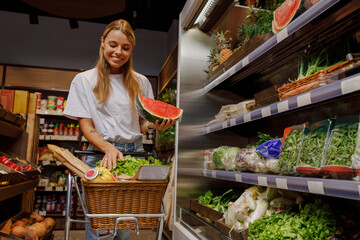 A very cheerful and happy woman joyfully holds a large, ripe watermelon while shopping for fresh, healthy vegetables