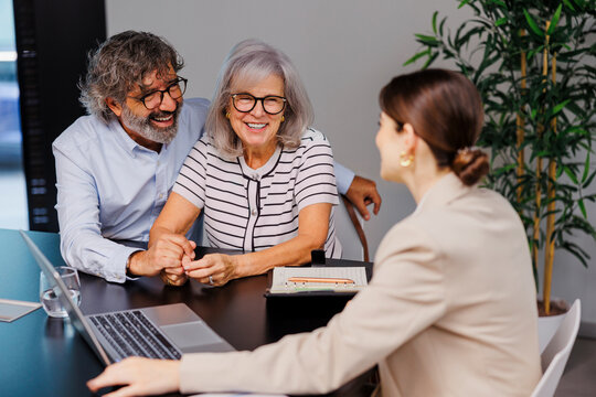 Happy senior couple holding hands while listening to financial advisor