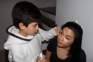 A child takes care of his mother by putting in eye drops