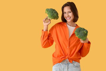 Beautiful young happy woman with fresh broccoli on yellow background. Diet concept