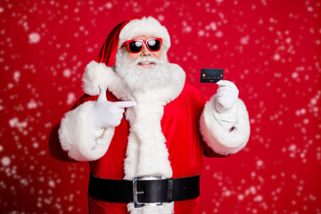 Portrait of his he nice handsome cheerful bearded Santa holding in hand demonstrating card shop cash pay payment presentation isolated bright vivid shine vibrant red color background