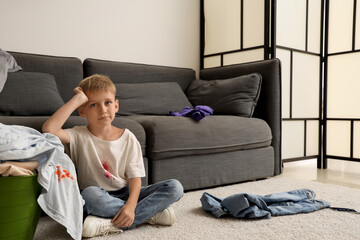 Little boy in stained t-shirt sitting on floor with laundry basket at home