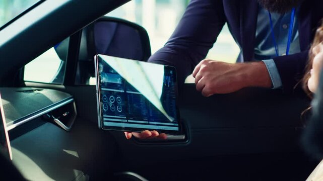 Showroom salesperson showing stat charts on tablet to clients after they finished test drive to persuade them. Dealership agent showing vehicle driving metrics graphs on device to couple, camera A