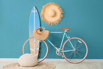 Surfboard, straw hat, pouf and bicycle near blue wall in room