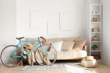 Sofa with cushions, plaid, shelving unit and bicycle near white wall in living room