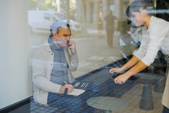 Businessman talking on phone taking notes in coffee shop