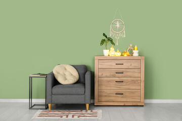 Interior of living room with armchair and glowing pumpkins on commode