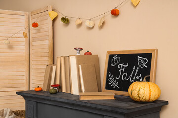 Naklejka premium Chalkboard with books and autumn decorations on modern fireplace near beige wall