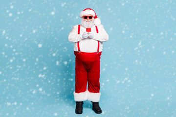 Full length photo of modern style funny funky fat santa claus with big abdomen use cellphone search winter season sales wear white overalls red stylish suspenders isolated over blue color background