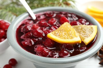 Tasty cranberry sauce in bowl and orange on table, closeup