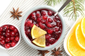 Tasty cranberry sauce in bowl, berries, orange, anise and fir branches on white wooden table, top view