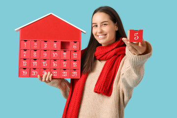 Happy young woman with Christmas advent calendar on blue background