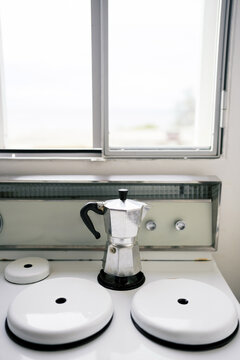 Silver Moka pot on stovetop under bright window light.