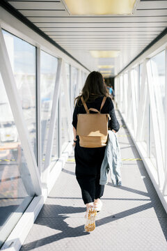 Woman walks down a brightly lit airport jet bridge.