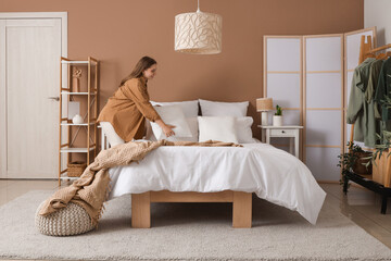 Pretty young woman making bed in modern bedroom