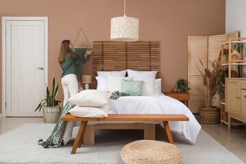 Pretty young woman decorating wall in bedroom